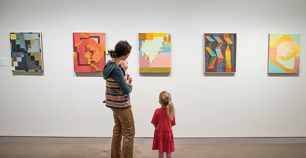 A woman and two young children observe abstract paintings displayed on a gallery wall in Bangor, Maine.