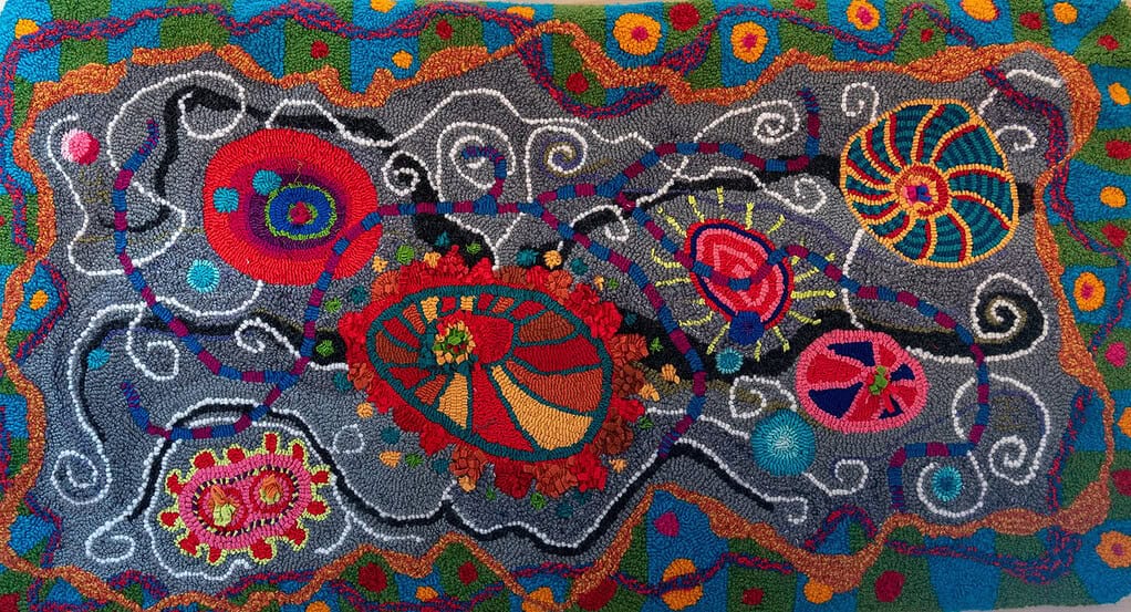A colorful, abstract textile artwork featuring various shapes, patterns, and vibrant colors, including swirling lines, circular forms, and intricate details, resembling a cosmic or cellular scene as part of Maine's fiber arts community.