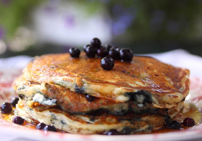 A stack of pancakes topped with fresh blueberries and drizzled with syrup on a plate.