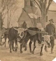A sepia-toned image of two oxen pulling a cart with two people. A person walks alongside in a snowy village setting.
