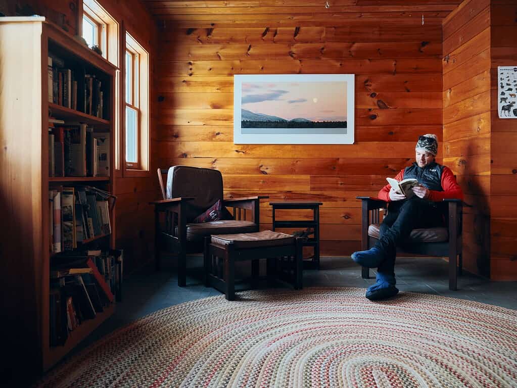 man sitting in a wood-paneled cabin reading a book