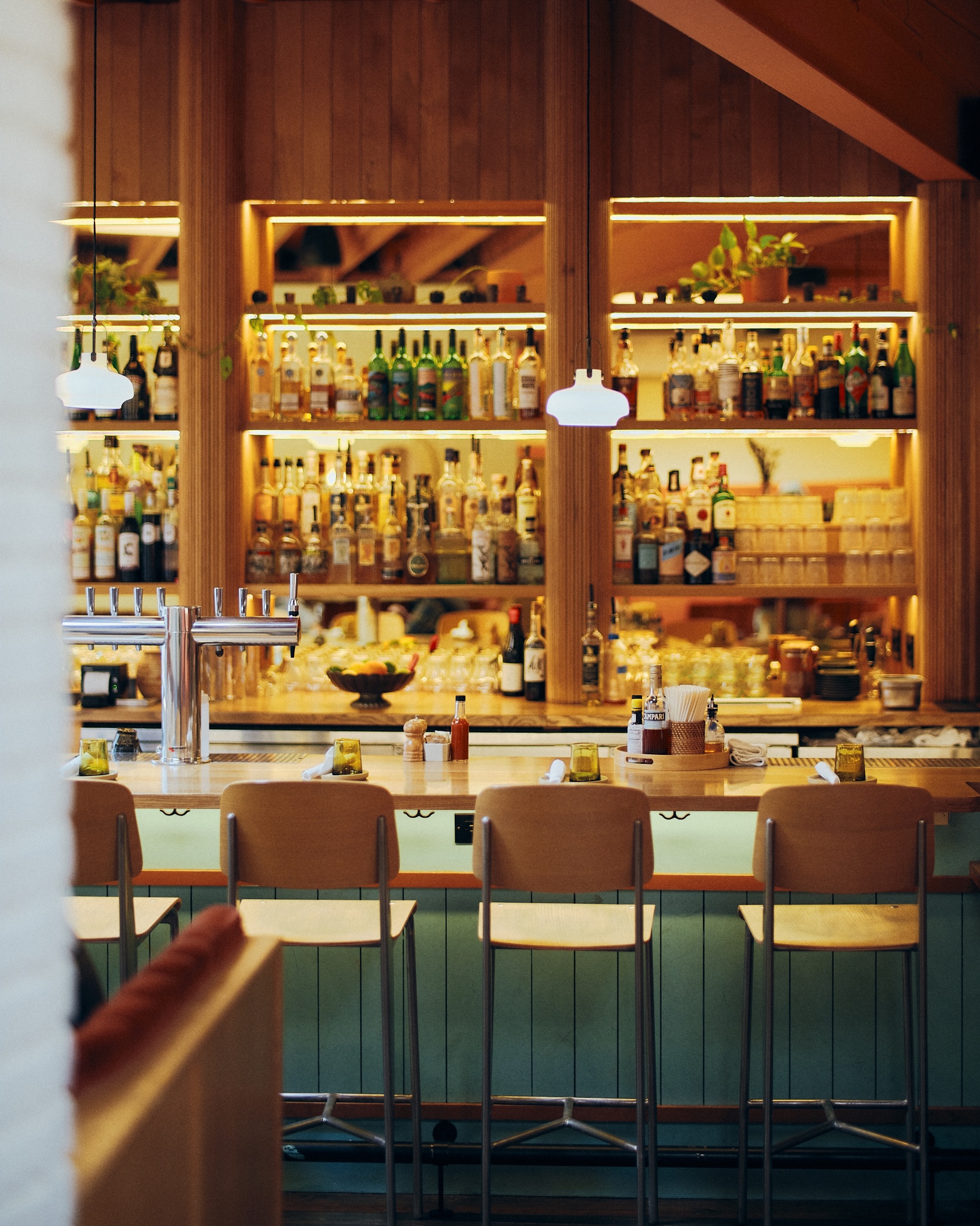 illuminated bar with midcentury modern chairs and alcohol bottles along the back wall