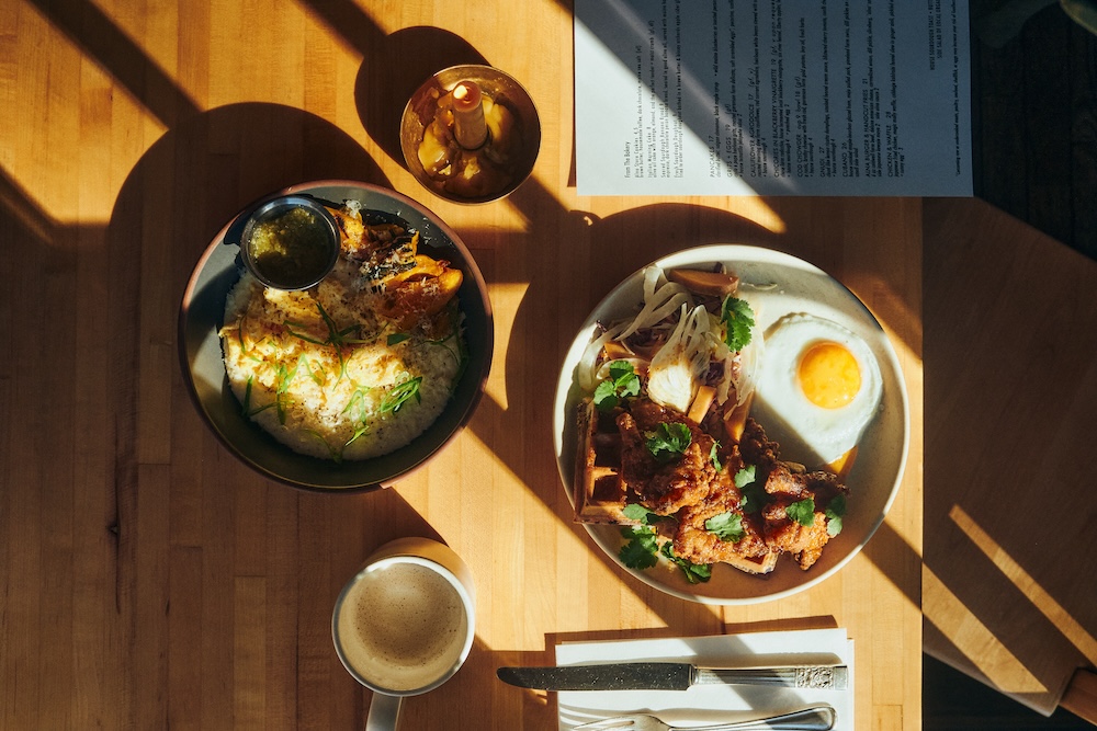 overhead image of a plate of fried chicken, waffles and eggs with coffee and early sunlight across the table