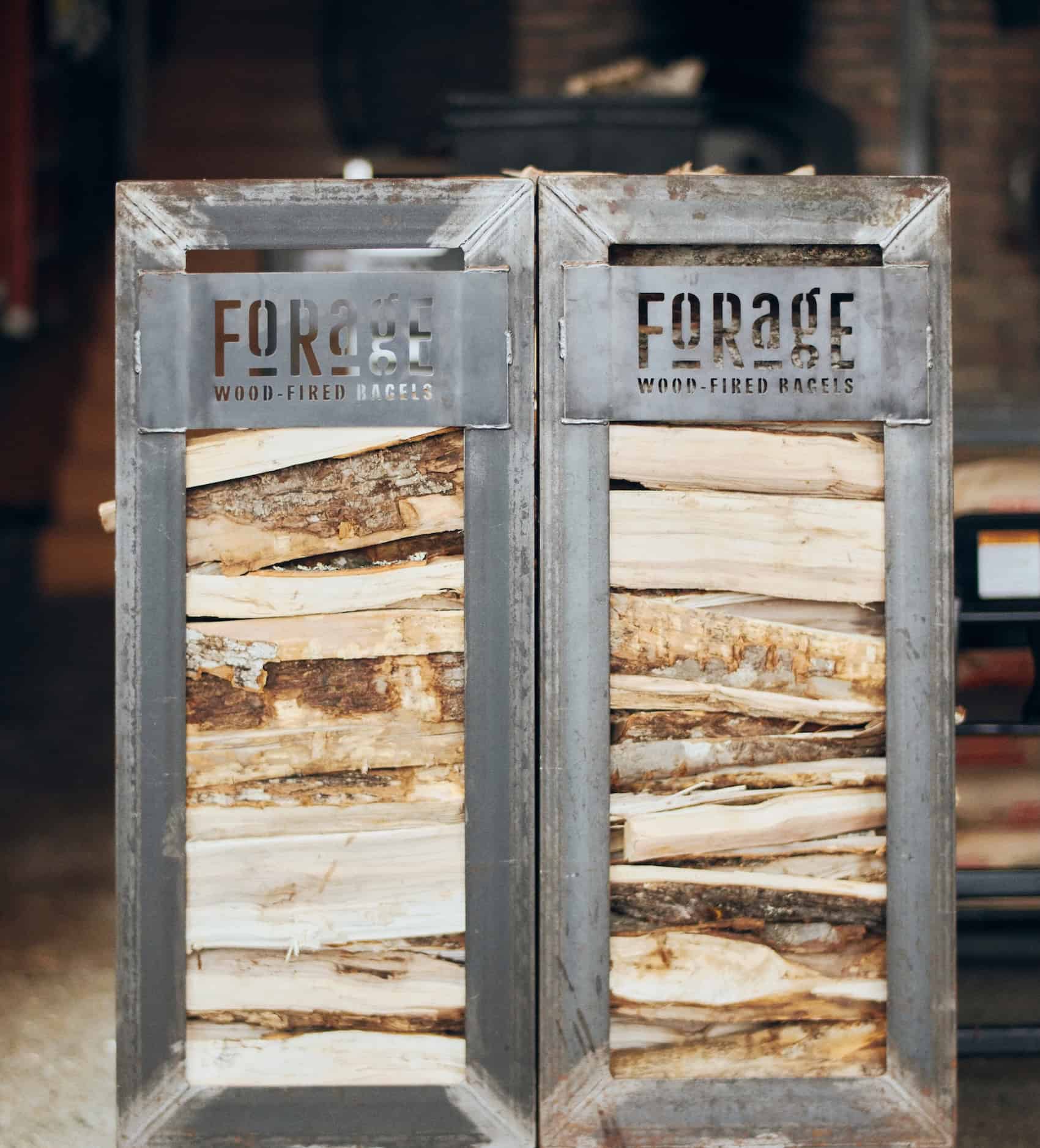 stack of firewood with a metal sign that says Forage Wood-Fired Bagels
